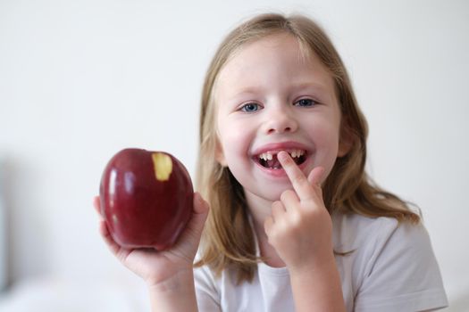 Portrait of joyful child girl without teeth holds apple. Change of milk teeth and hard food concept
