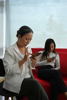 Mature asian businesswoman sitting in cooperate office and using mobile phone.