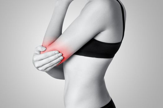 Closeup view of a young woman with elbow pain on gray background. Black and white photo with red dot.