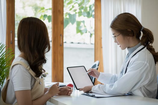 Side view female doctor in white coat holding digital tablet and explaining diagnosis to patient.