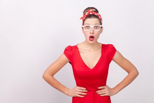 Expressive surprised woman, open mouth with shock, looking at camera. Indoor, studio shot, isolated on gray background