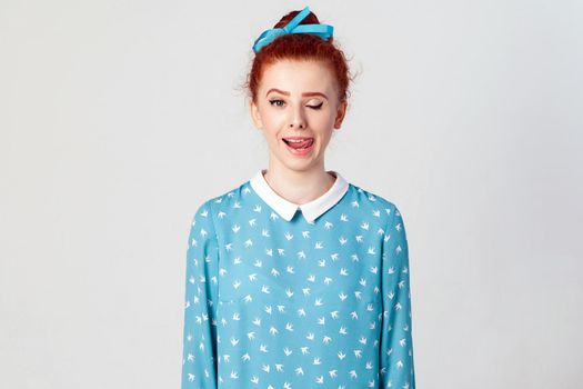 Young teenage girl with ginger hair knot sticking out her tongue having funny look isolated over gray background. Studio shot.