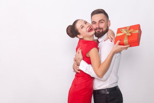 It's present for you! Couple hugging, woman holding gift box. Indoor, studio shot, isolated on gray background