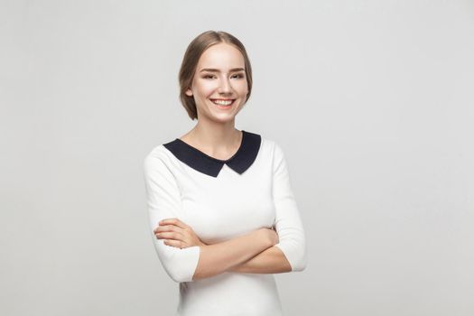 Businesswoman crossed hands, toothy smiling and looking at camera. Studio shot, gray background