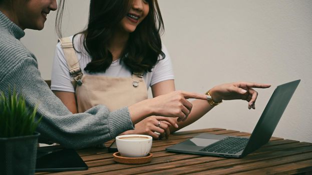 Cropped shot two smiling young asian women pointing on screen of computer laptop.