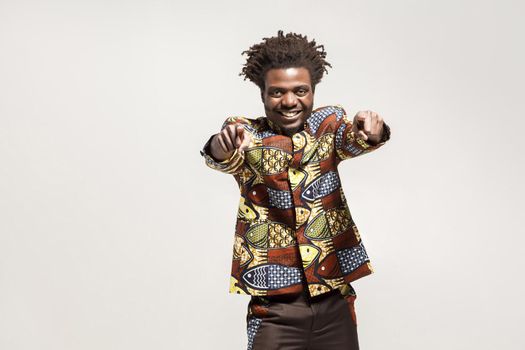 Emotion african man, toothy smiling pointing fingers at camera. Indoor, isolated on gray background