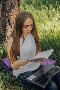 the girl sits on the grass and uses a laptop. Education, lifestyle, technology concept, outdoor learning concept.