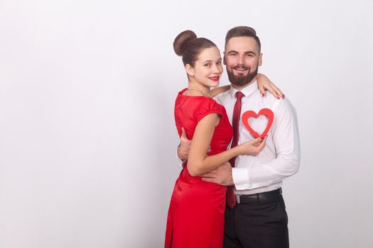 Young couple celebrate valentines day, hugging and toothy smile. Indoor, studio shot, isolated on gray background