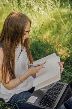 On the banner, a young girl works with a laptop in the fresh air in the park, sitting on the lawn. The concept of remote work. Work as a freelancer. The girl takes courses on a laptop and smiles