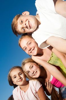 four happy beautiful children looking at camera from top in the sunny summer day and blue sky. looking at camera with funny face and toothy smile. view from below.