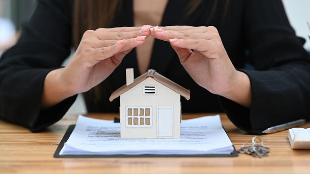 Cropped image of woman hands sheltering small house model. Real estate, leasing insurance, purchase and maintenance concept.