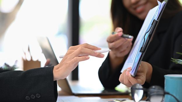 Cropped view of professional business people discussing project statistics or financial report together at office desk.