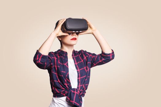 Young beautiful woman in casual style with virtual reality headset on beige background. studio shot. .