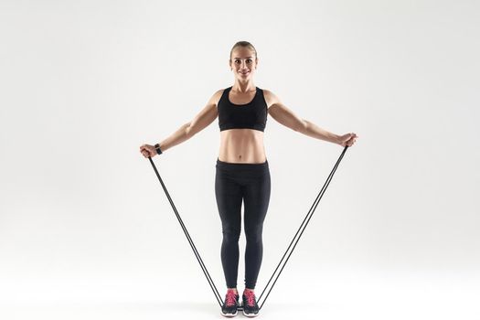 TRX training. Activity happiness woman holding skipping rope, toothy smiling and looking at camera. Studio shot, gray background