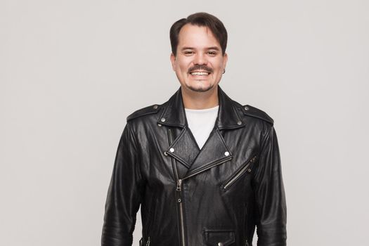 Happiness adult man in leather jacket, looking at camera and toothy smile. Indoor shot in gray background