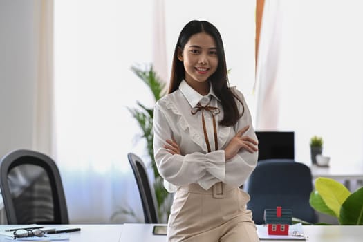 Confident young businesswoman standing with crossed arms at modern office.