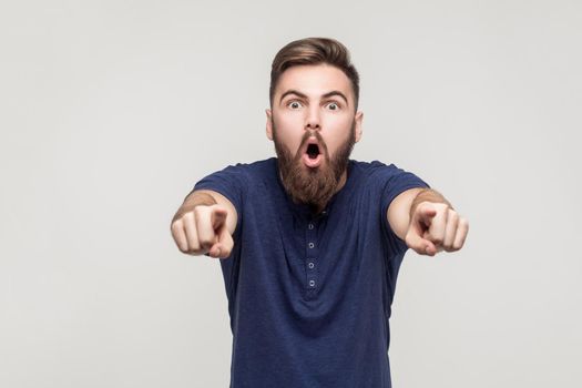 Hey you! Amazement bearded man pointing fingers at camera with open mouth and big eyes. Studio shot