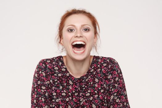 Showing teeth. Beautiful redhead woman open mouth and showing white and healthy teeth. Isolated on gray background