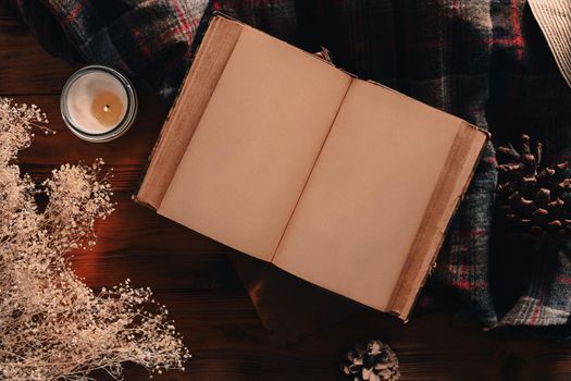 Top view vintage book, candle and pine cones on wooden background.