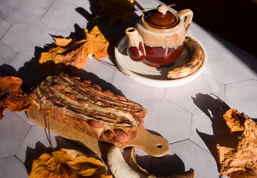 Still life Banana pie with a ceramic teapot in the rays of the autumn sun on a gray tile table. High quality photo