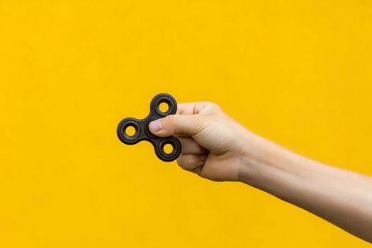 human hand holding black fidget spinner on yellow background..