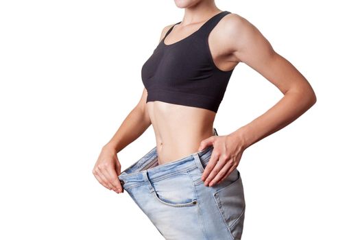 Close-up of slim waist of young woman in big jeans showing successful weight loss, isolated on white background, diet concept.