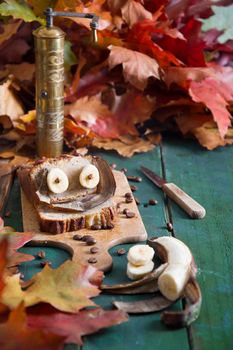 Creative still life of banana cake with eyes on a background of bright autumn leaves, copper coffee grinder and ceramic cup with coffee on a wooden background. High quality photo