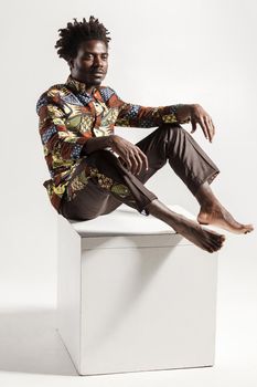 Famous and fashion african man posing on cube. Indoor, isolated on gray background