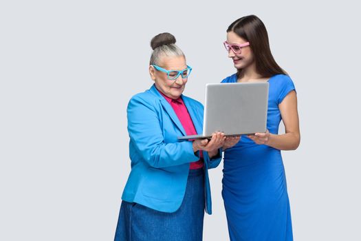 happy grandmother education or woman for work in social networking. granddaughter trying to teach her grandma to use laptop and working on internet. indoor, studio shot, isolated on gray background.