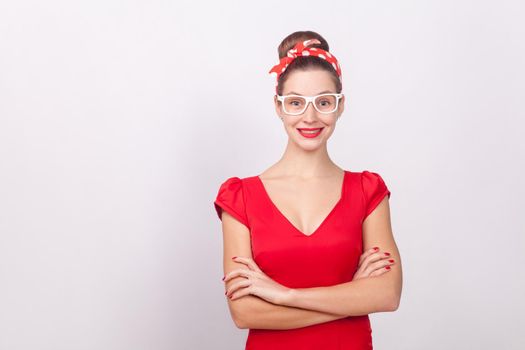 Cheerful beautiful woman in red dress and white glasses smiling. Indoor, studio shot, isolated on gray background