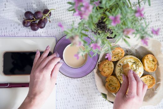 Lavender french breakfast, goat cheese and oven baked baguette, notepad, smartphone, flat lay food, female hand dipping slice of bread in cheese. High quality photo