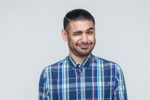 Emotional hipster man wink and smiling at camera. Good humans emotions and feelings. Studio shot, gray wall