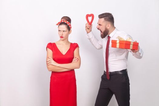 Conglict. Woman ignore man, businessman roar, holding gift and heart. Indoor, studio shot, isolated on gray background