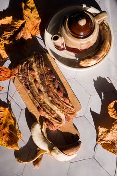 Still life Banana pie with a ceramic teapot in the rays of the autumn sun on a gray tile table. High quality photo