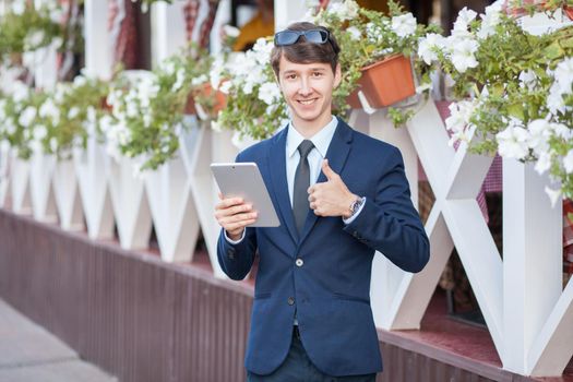 young man in business suit holding tablet on summertime day.