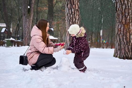 a woman in relation to her child or childrenCaring mother puts gloves on her child on a winter day.