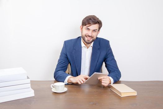 Technology, people and business concept - handsome man with beard and brown hair and blue suit and tablet pc computer and some books looking at camera with smile and holding tablet in the office. .Isolated on white background. .