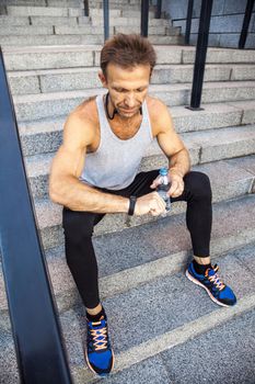 Sportsman with bottle of water is resting and checking his smart watch after running. fitness, sport, exercising and people healthy lifestyle concept.