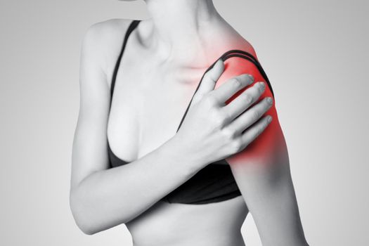 young woman with pain on her arm and shoulder on gray background. Black and white photo with red dot.