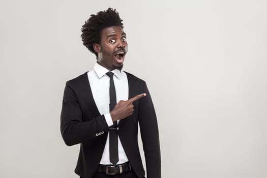 African businessman pointing finger at copy space, looking at camera with shocked face. Studio shot, gray background