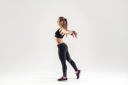 Profile blonde woman, holding skipping rope. Studio shot, gray background