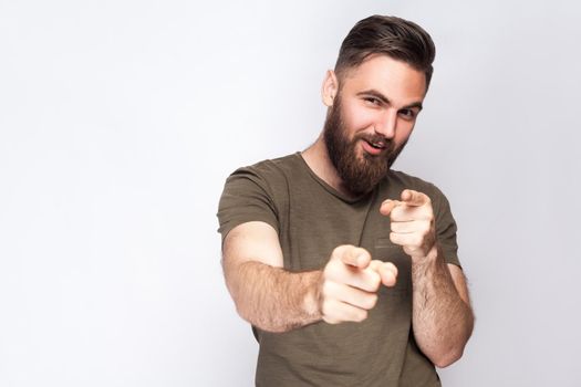 Hey you! Portrait of happy bearded man with dark green t shirt against light gray background. studio shot. .