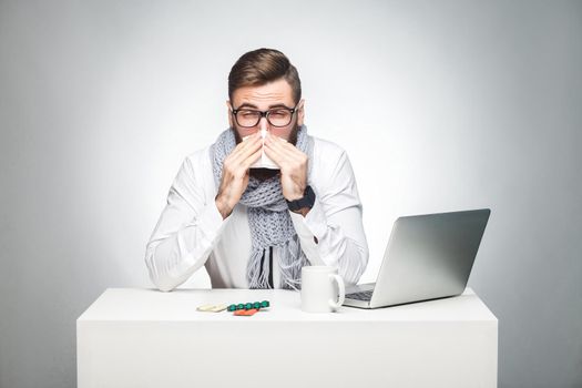 Portrait of sick scribble young boss in white shirt, scarf and black tie are sitting in office and need to finish important report, have grippe virus. Studio shot, isolated, gray background, indoor