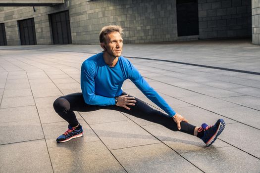 Handsome athlete man in black blue sport uniform stretching body, warming up and get ready for jogging.