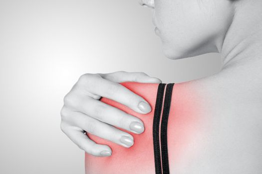 young woman with pain on her arm and shoulder on gray background. Black and white photo with red dot.