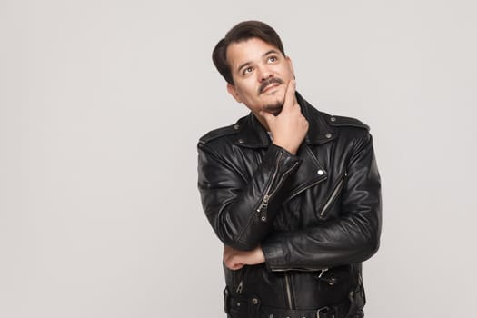 Indoor isolated studio shot on gray background of adult man looking away, having doubtful and indecisive face expression. Studio shot