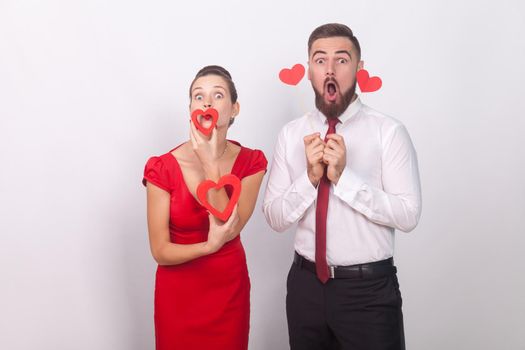 Expressive funny couple holding decorative sign love, heart symbol. Indoor, studio shot, isolated on gray background