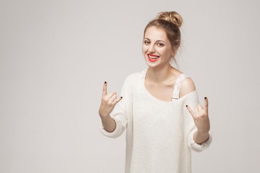 Rock and roll sign. Happiness woman showing rock sign at camera. Studio shot, isolated on gray background