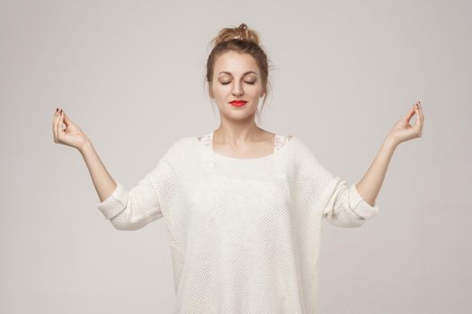 Blone young adult woman closed up, relax and doing youga asana. Studio shot, gray background