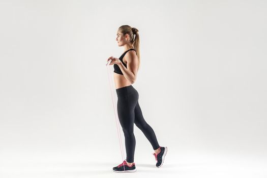 Side view. Attractive woman holding skipping rope and looking forward. Studio shot, gray background